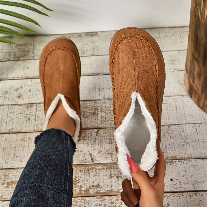 Brown slippers with white lining worn by a person on a wooden floor.