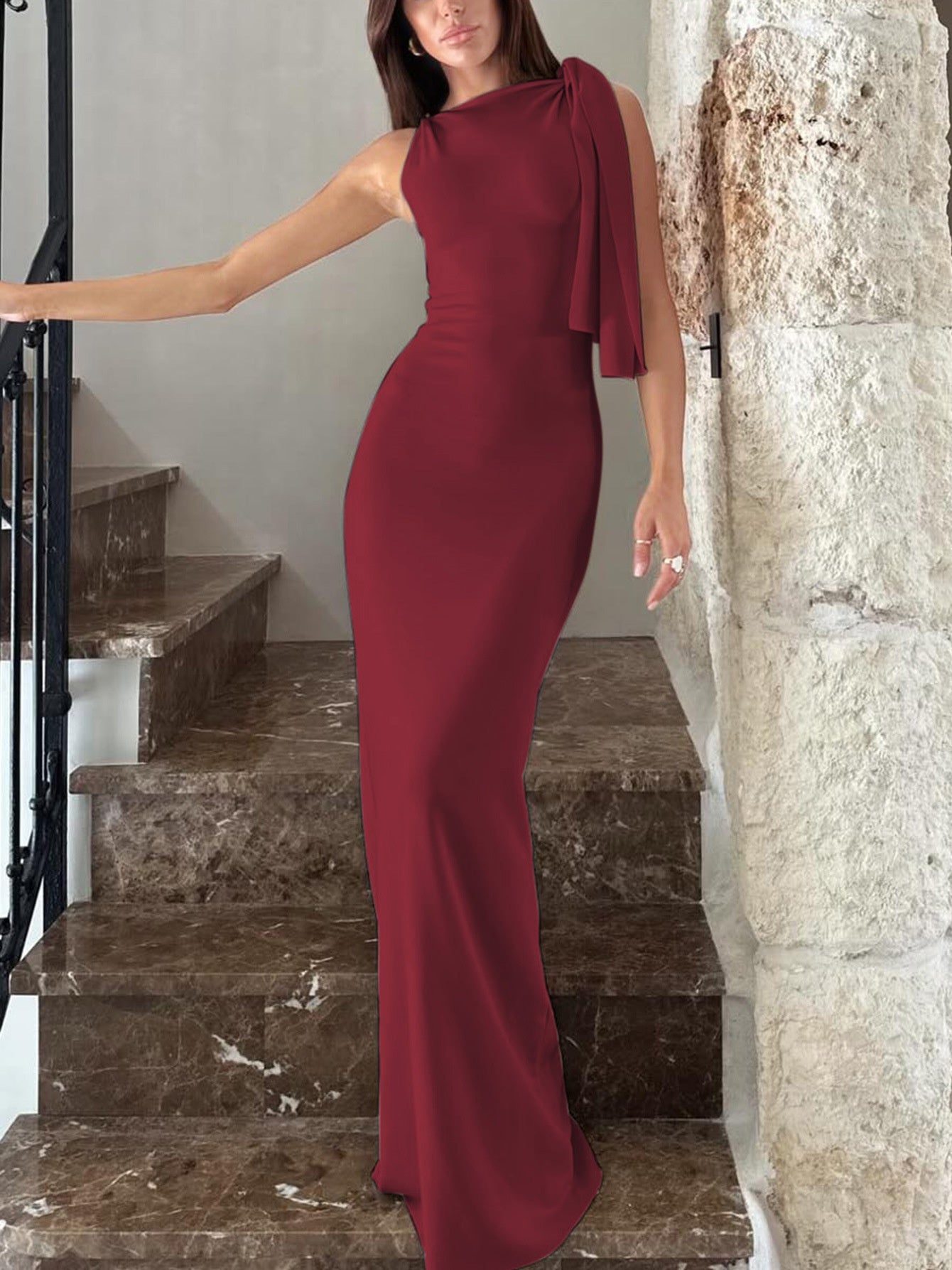 Woman in a burgundy evening gown standing on marble steps.