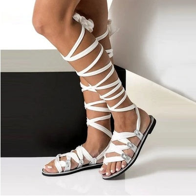 White strappy sandals worn by a person on a neutral background