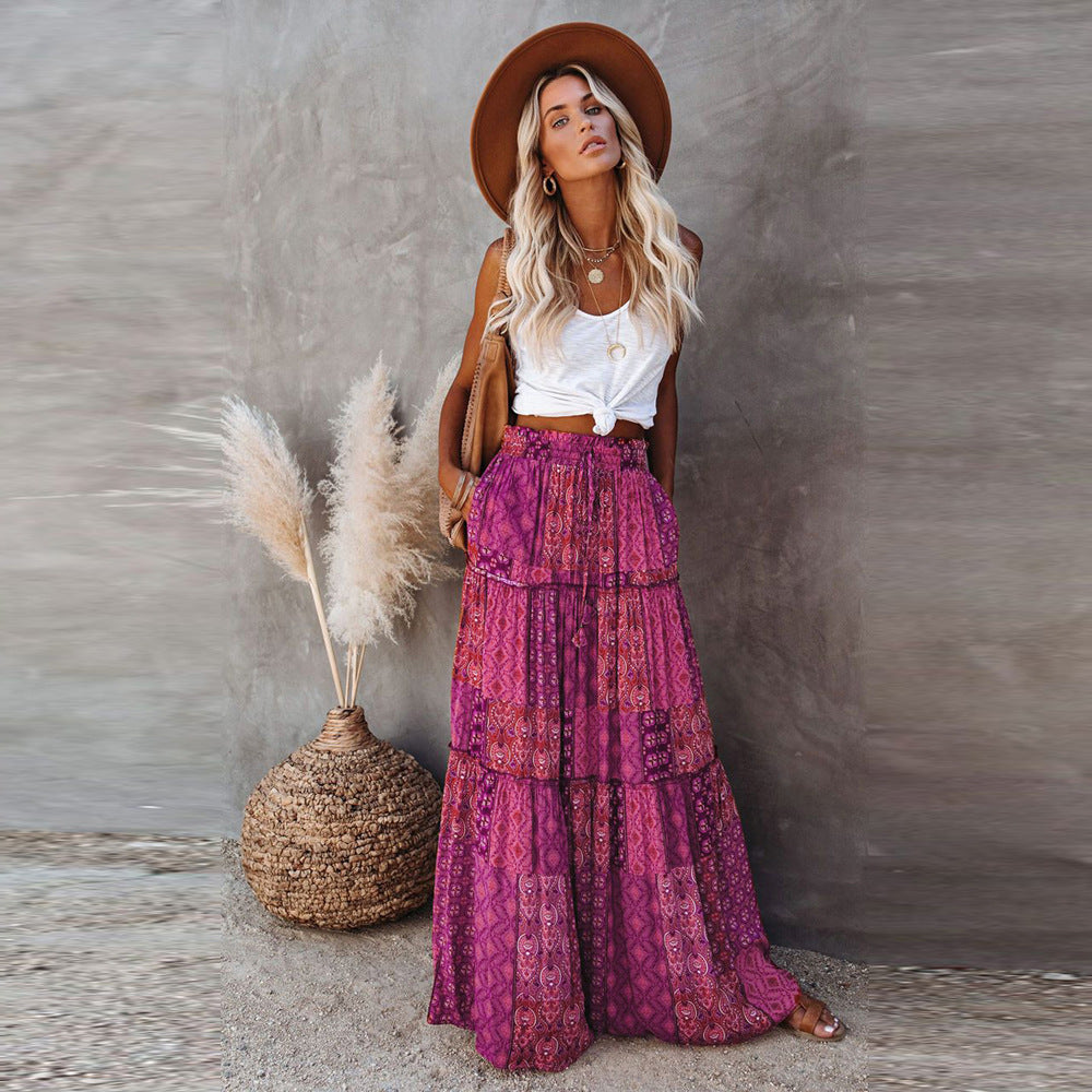 Woman in a white top and purple patterned skirt standing next to a woven basket with dried plants against a gray wall.