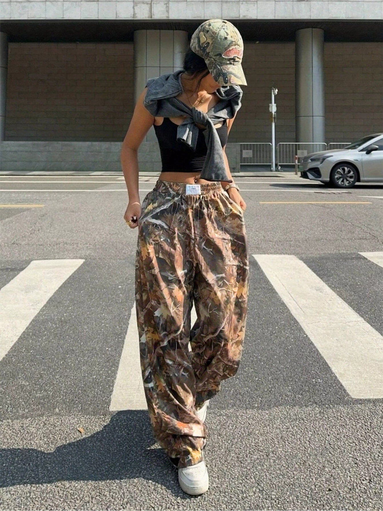 Person wearing camouflage pants and a cap on a city street.