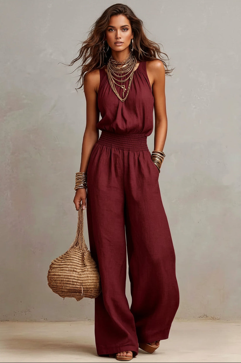 Woman wearing a burgundy jumpsuit holding a woven bag against a plain background
