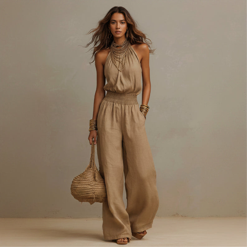 Woman wearing a beige jumpsuit holding a woven bag against a neutral background