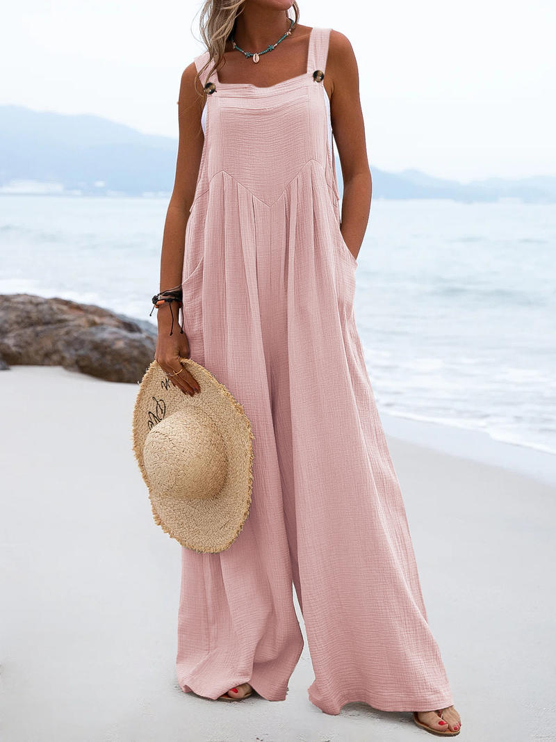 Woman in a pink dress holding a straw hat on a beach