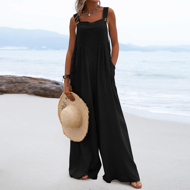 Woman in a black dress holding a straw hat on a beach