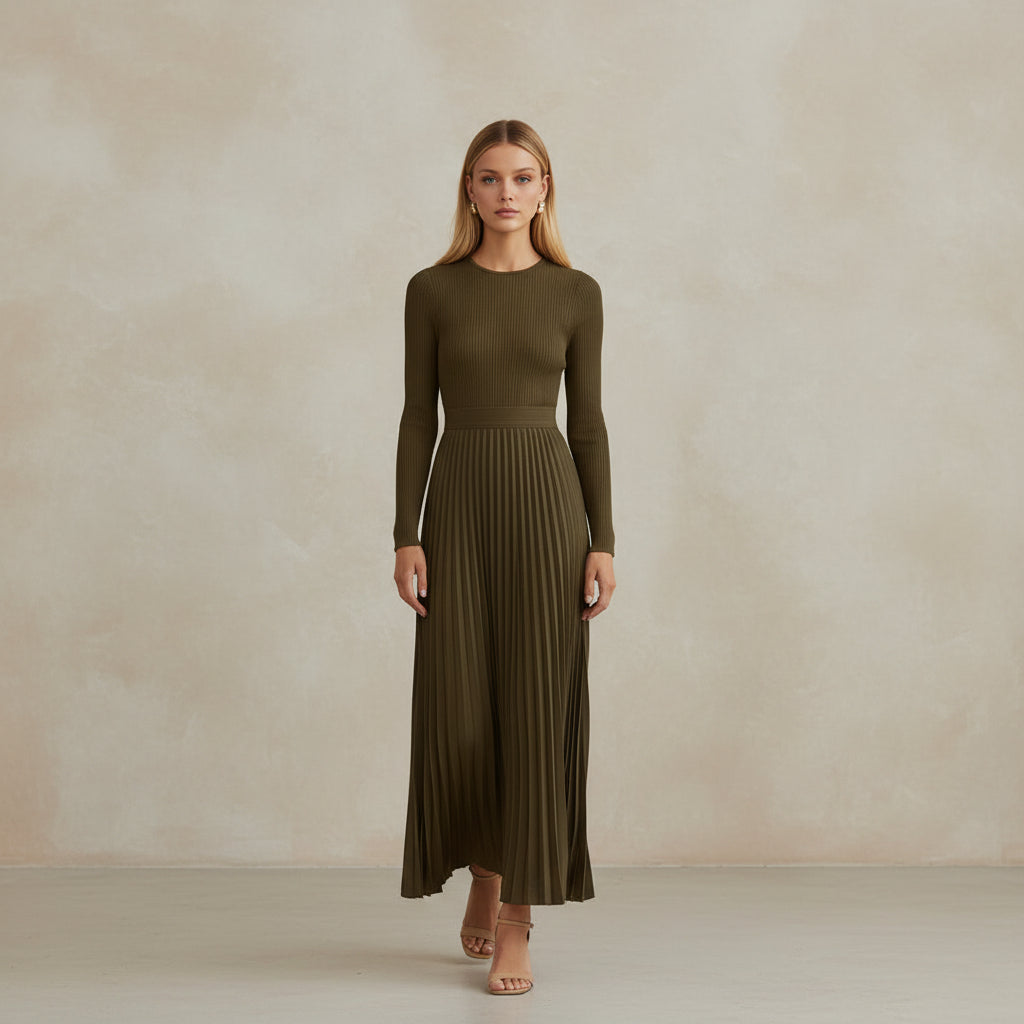 Woman in a long green dress holding a beige handbag against a stone wall.