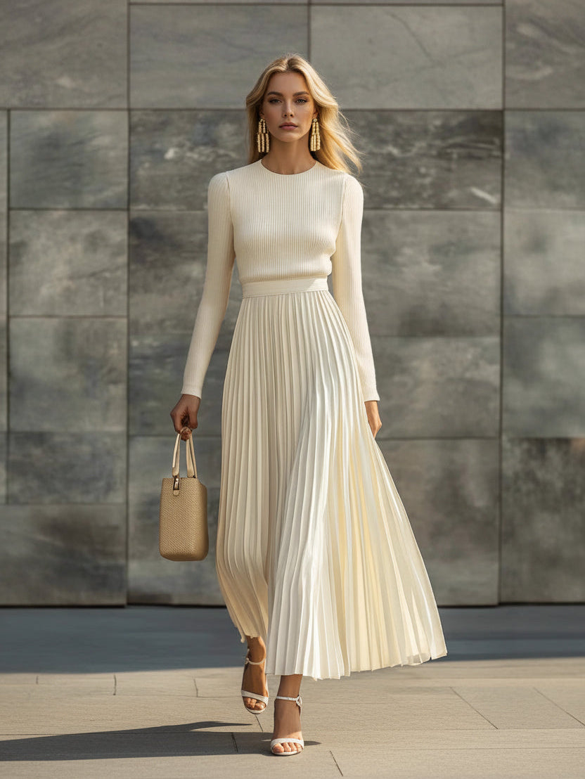 Woman in a long beige dress holding a matching handbag against a stone wall.