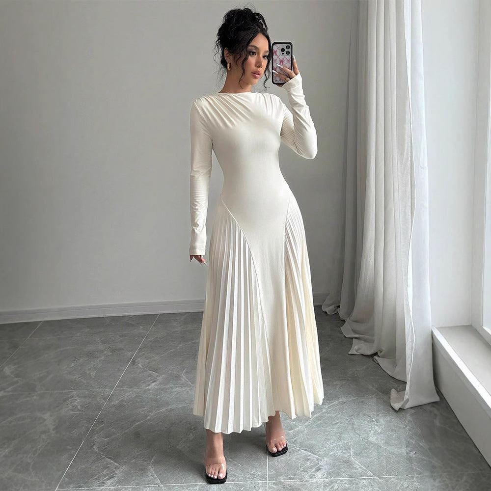 Woman in a white pleated dress taking a mirror selfie in a room with light gray walls and white curtains.