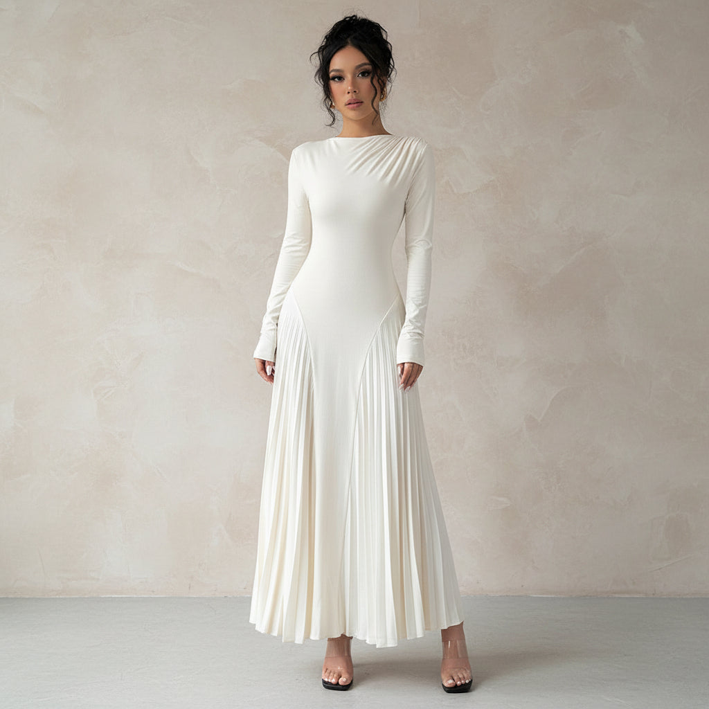 Woman wearing a white pleated dress standing in a room with curtains and a gray floor.