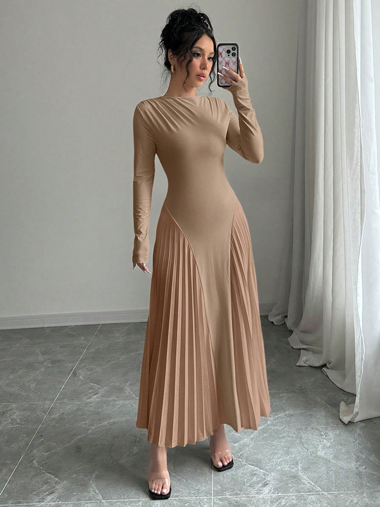 Woman taking a mirror selfie wearing a beige long-sleeve dress in a room with light gray walls and white curtains.