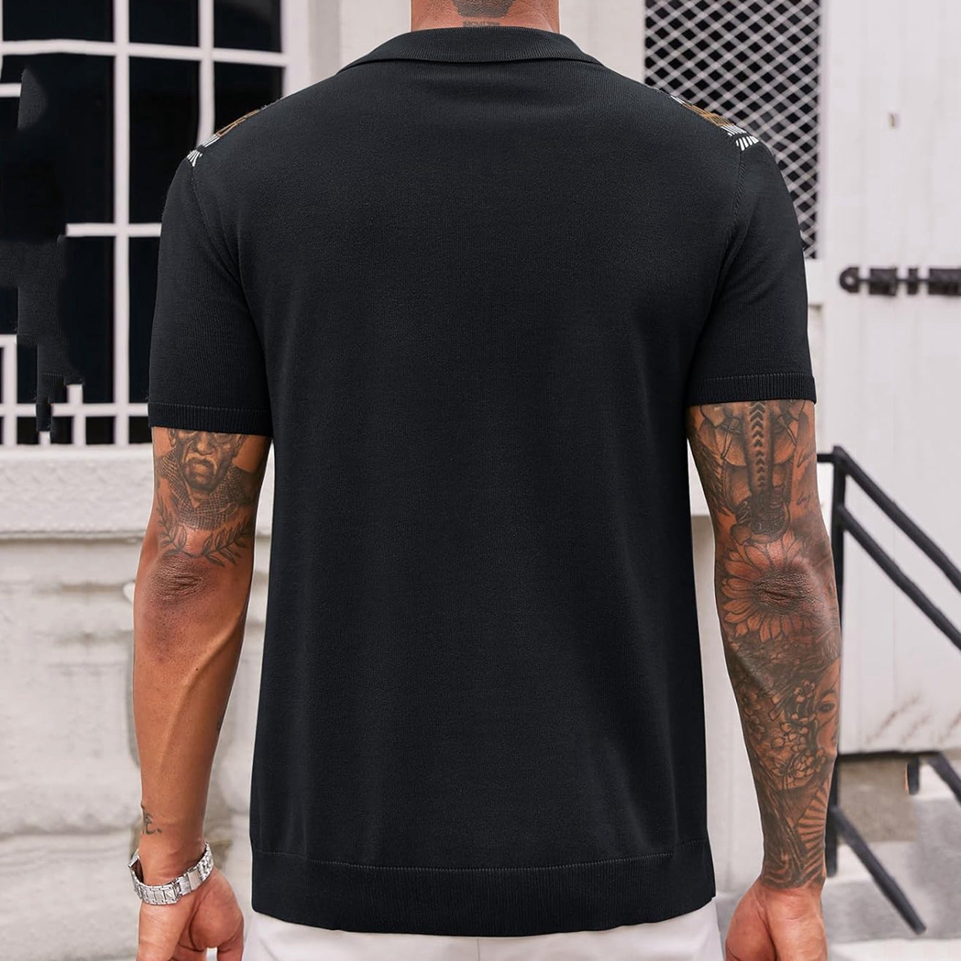 Person wearing a black polo shirt with visible tattoos on arms, standing outdoors.