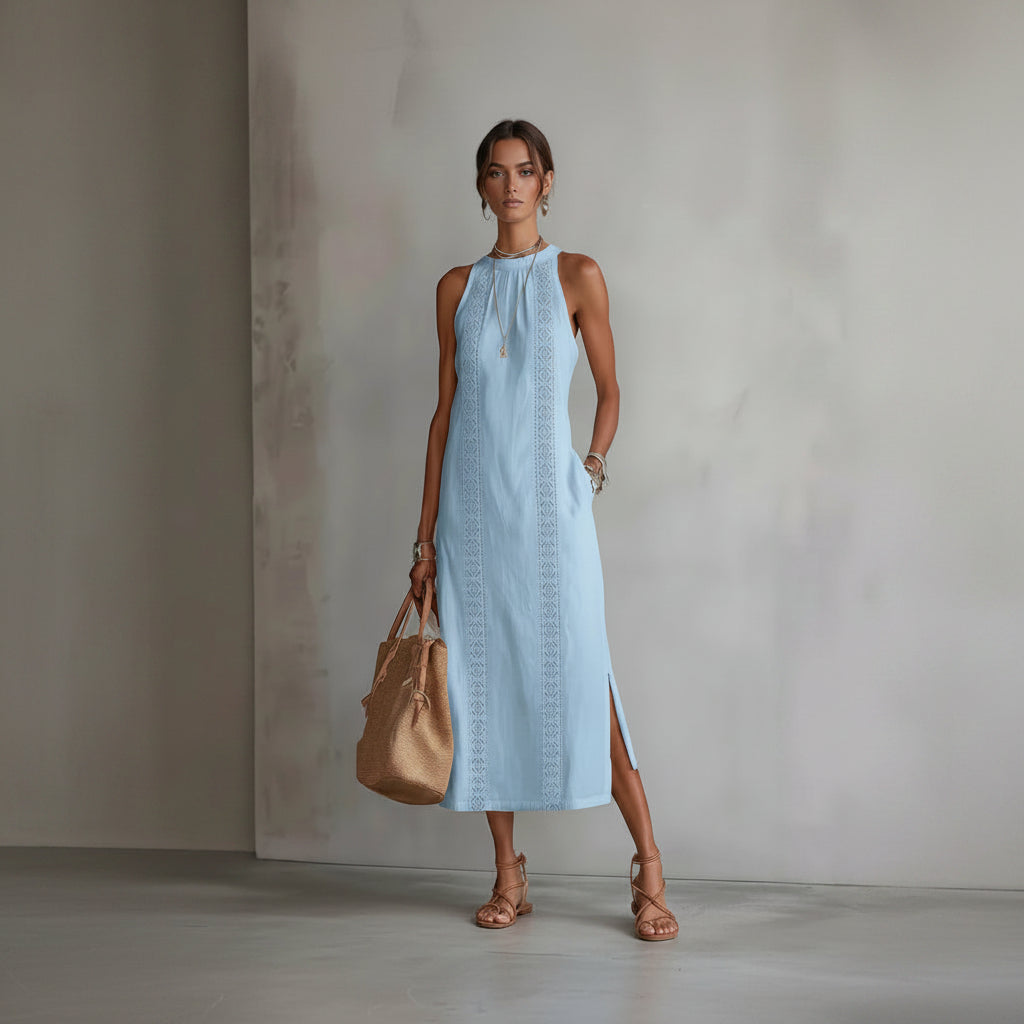 Woman wearing a light blue dress with intricate patterns, holding a beige handbag against a neutral background.
