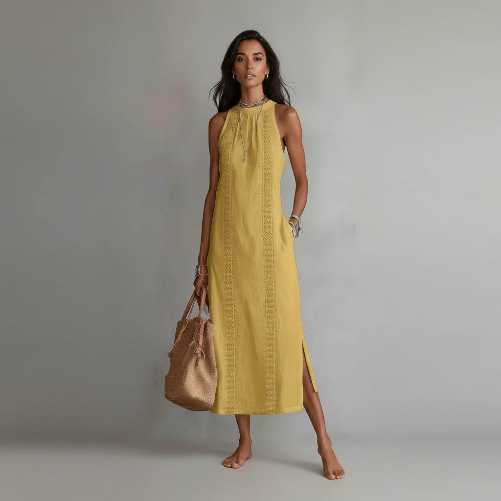 Woman wearing a yellow dress with intricate patterns, holding a brown handbag against a plain background.