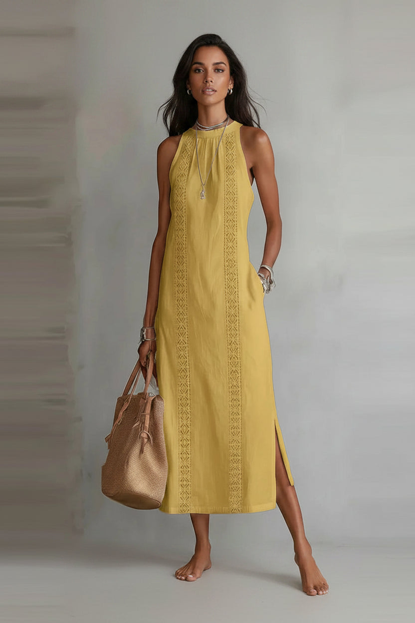 Woman wearing a yellow dress with intricate patterns, holding a brown handbag against a plain background.
