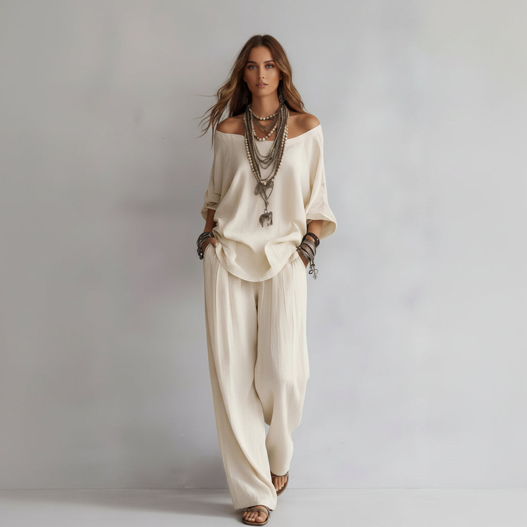 Person wearing a loose-fitting beige outfit with layered necklaces on a plain background