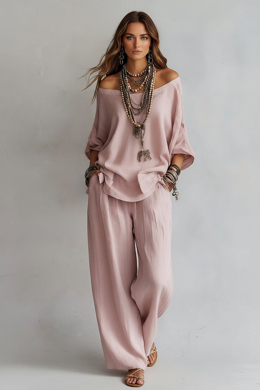 Person wearing a loose-fitting pink top and pants with layered necklaces and bracelets on a plain background