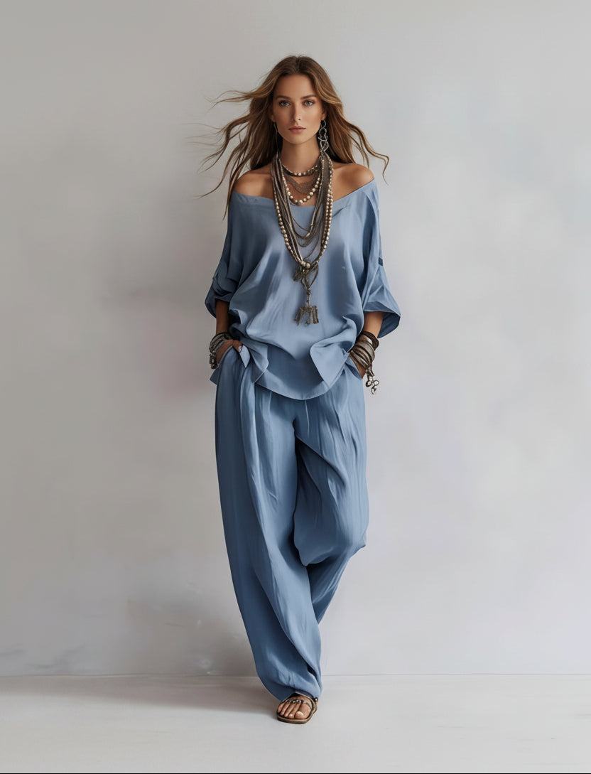 Woman wearing a blue outfit with wide-leg pants and off-shoulder top on a plain background