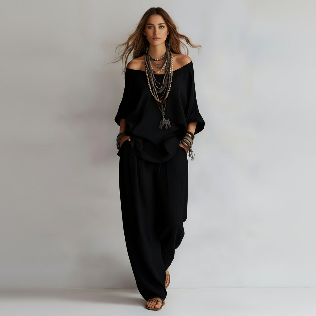 Person wearing a black outfit with layered necklaces on a plain background