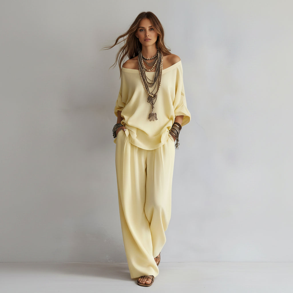 Person wearing a light yellow outfit with layered necklaces on a plain background