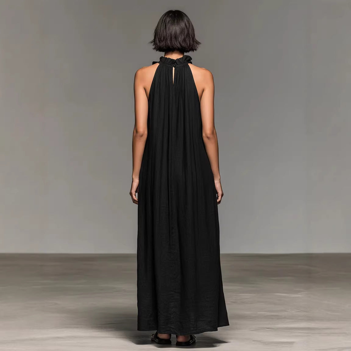 Woman wearing a black halter neck dress against a plain background