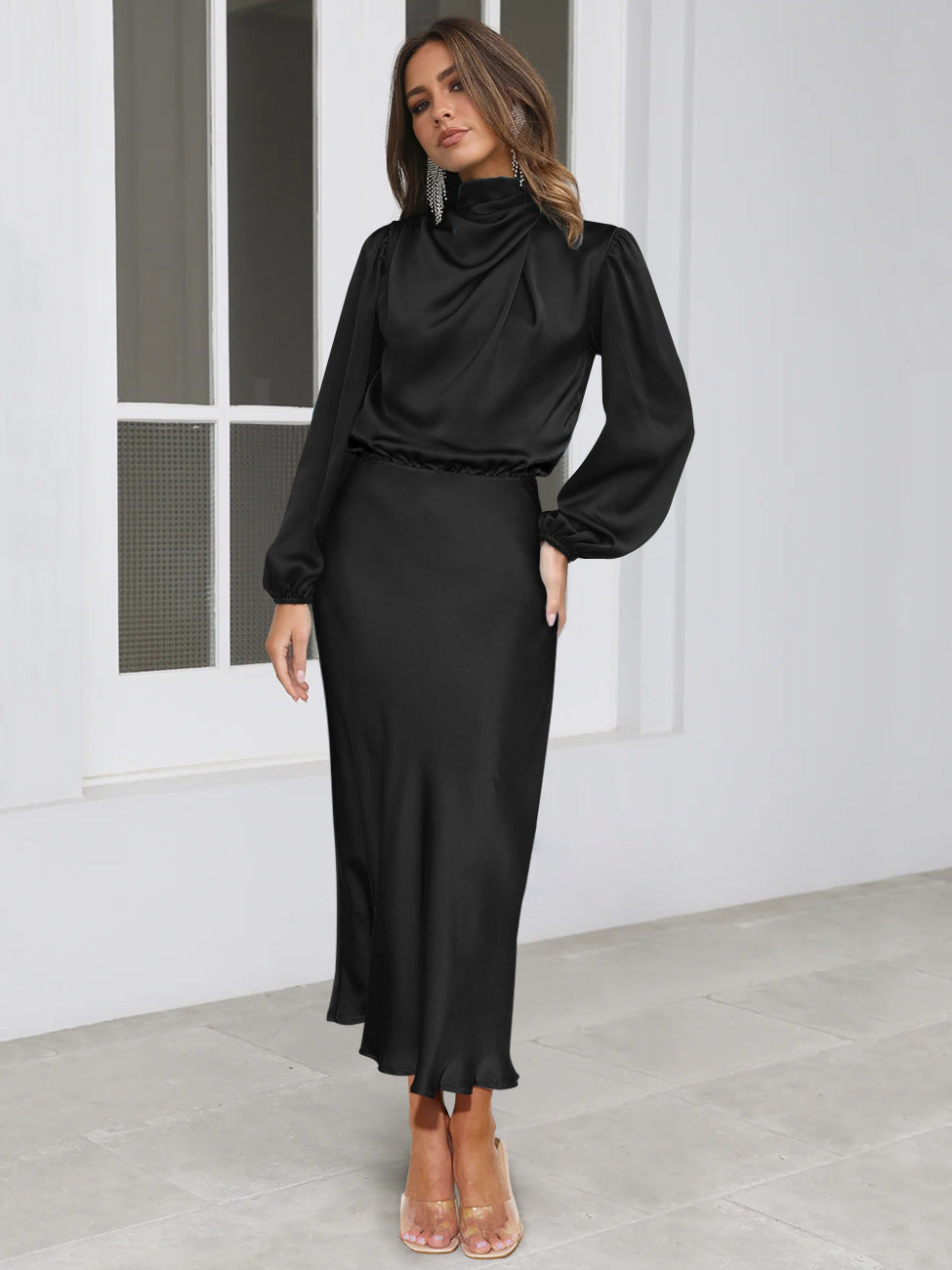 Woman wearing a black outfit standing in a minimalistic room.