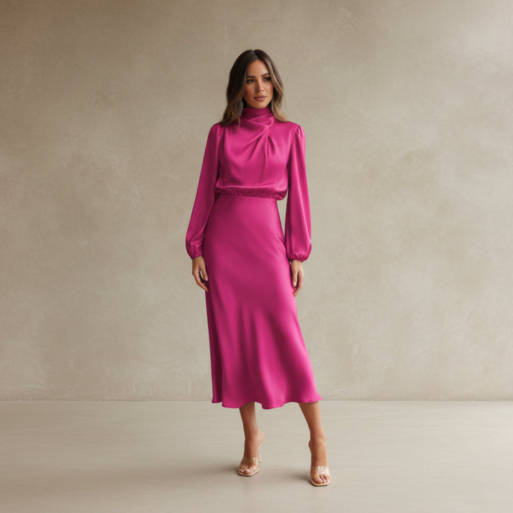 Woman wearing a pink dress standing against a white wall.