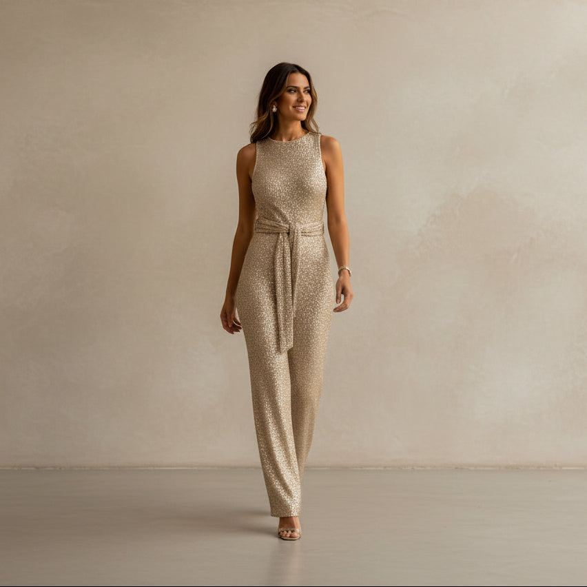Woman wearing a sparkly gold jumpsuit against a beige wall.