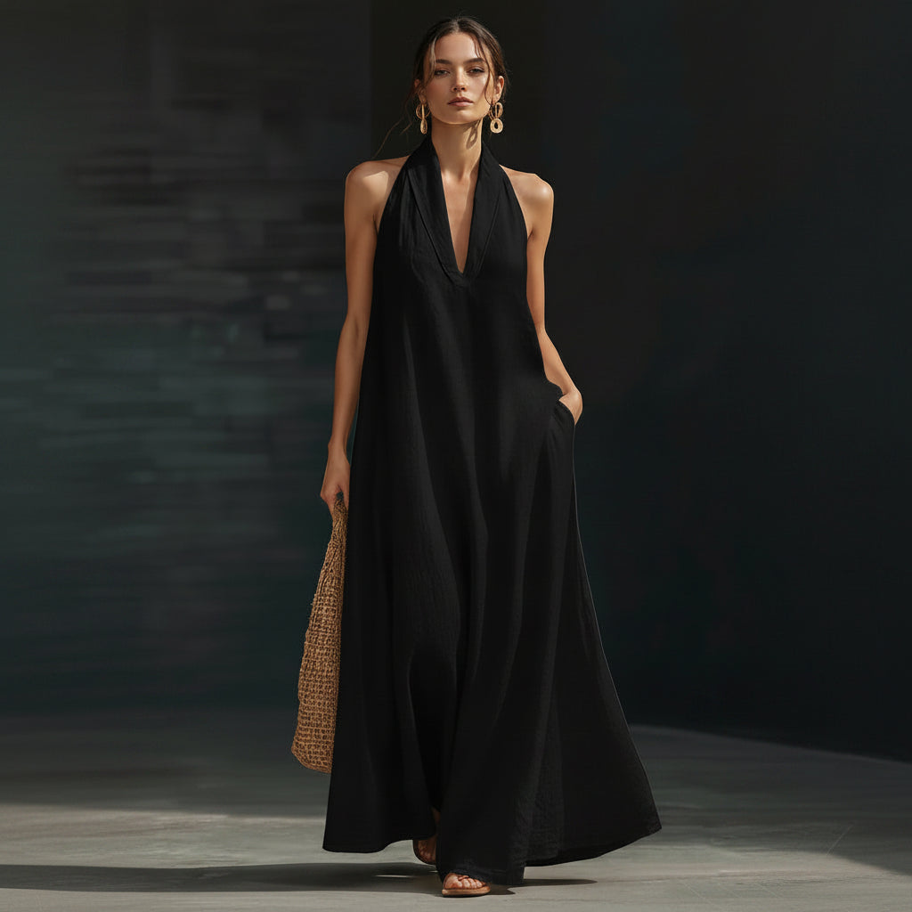 Woman wearing a black halter neck dress holding a woven bag against a dark background