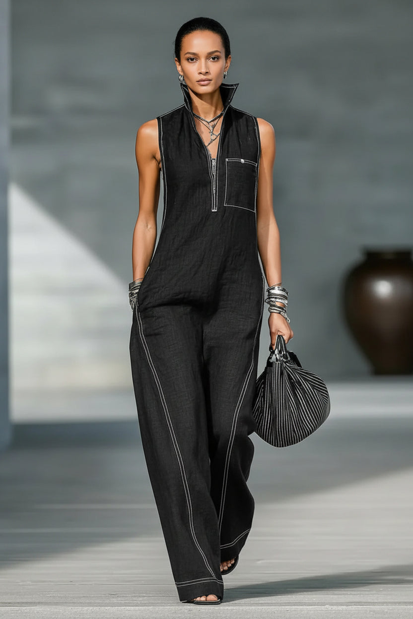 Person wearing a black sleeveless jumpsuit holding a black handbag in an indoor setting.