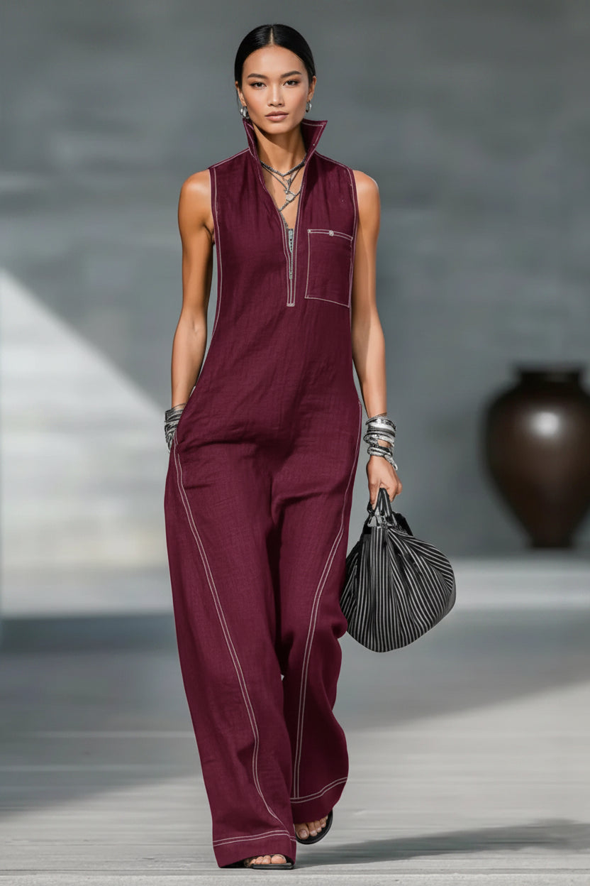 Woman in a burgundy jumpsuit holding a black handbag on a gray background