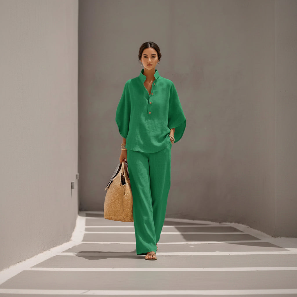 Person wearing a green outfit holding a straw bag against a gray wall.