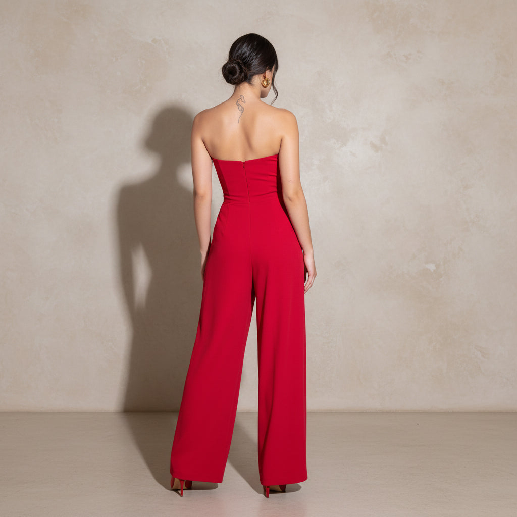 Person wearing a red strapless jumpsuit standing outdoors on a stone pavement.