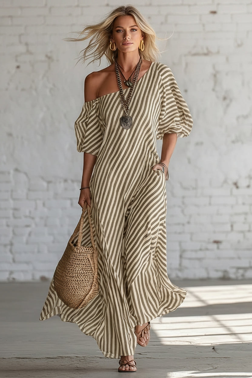 Woman wearing a striped dress with a woven bag against a white brick wall.