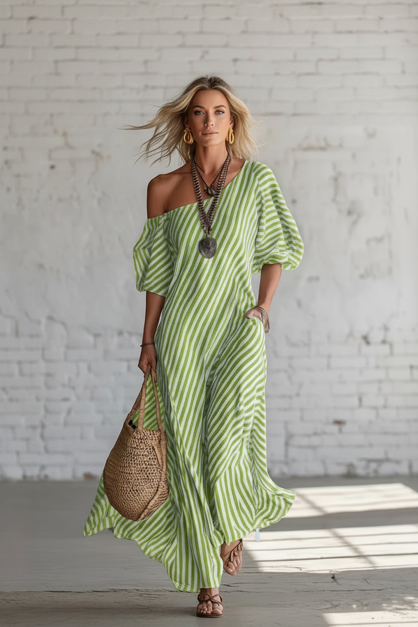 Woman wearing a green and white striped dress holding a woven bag against a white brick wall.