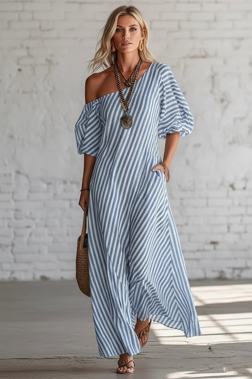 Woman wearing a blue and white striped dress holding a woven bag against a white brick wall.