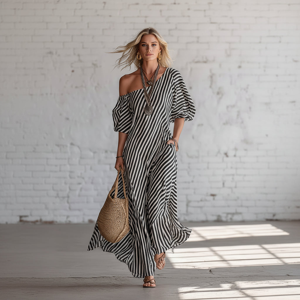 Woman wearing a black and white striped dress holding a woven bag against a white brick wall.