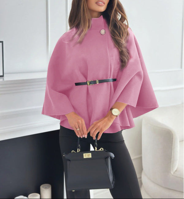 Woman wearing a pink cape and holding a black handbag indoors.