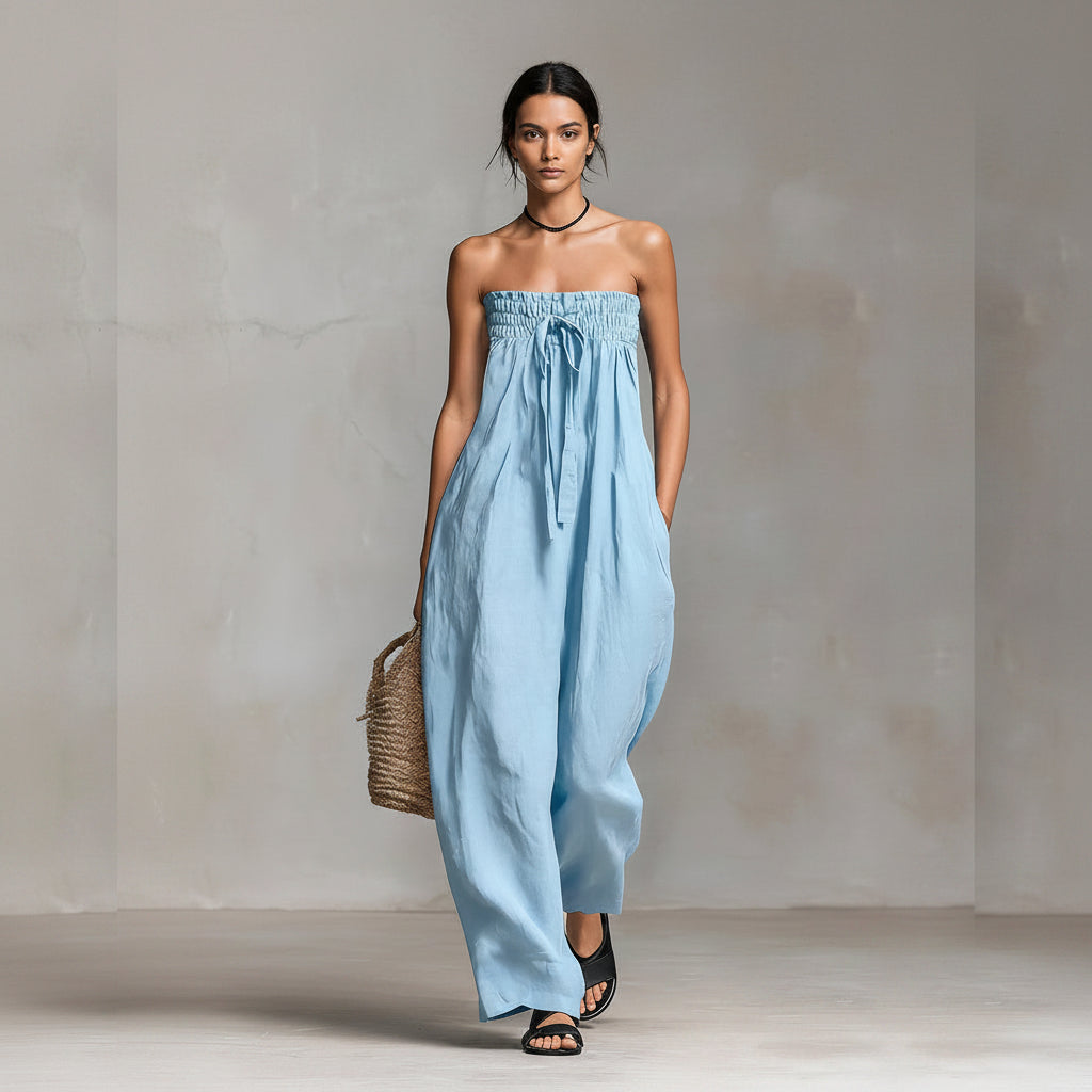 Woman wearing a light blue strapless jumpsuit holding a woven bag against a neutral background