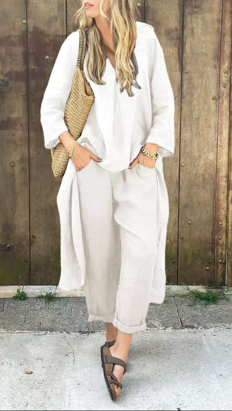 Woman wearing a white outfit with wide-leg pants and sandals, standing against a wooden fence.