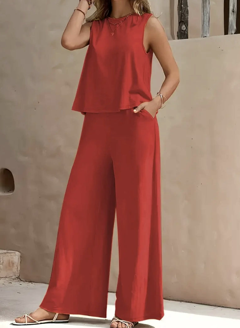 Person wearing a red sleeveless top and wide-leg pants against a beige wall.