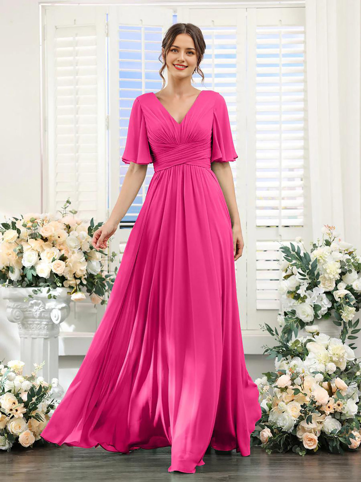 Woman in a pink dress standing in front of floral decorations with white shutters in the background.