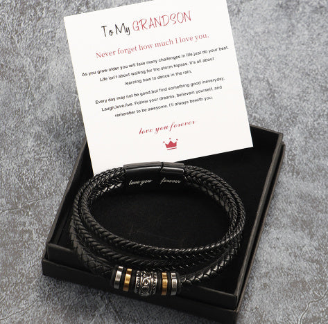 Black braided leather bracelet with gold accents in a black box with a card on a gray surface