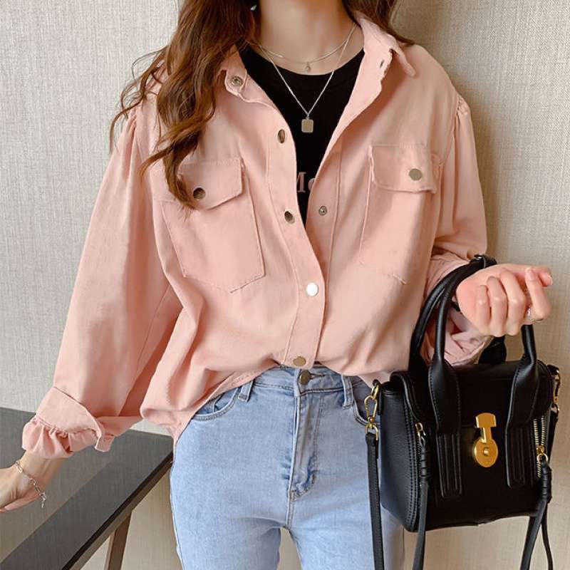 Person wearing a pink jacket and blue jeans, holding a black handbag against a neutral background