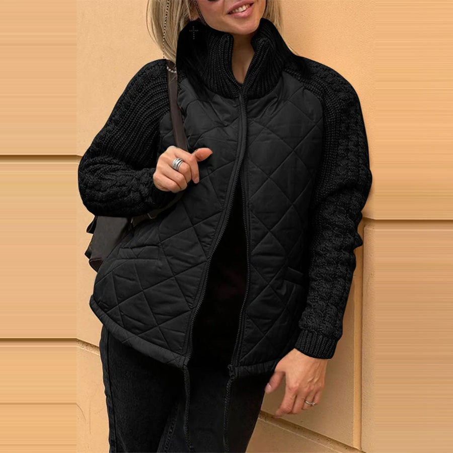 Person wearing a black quilted vest over a black sweater against a beige wall.