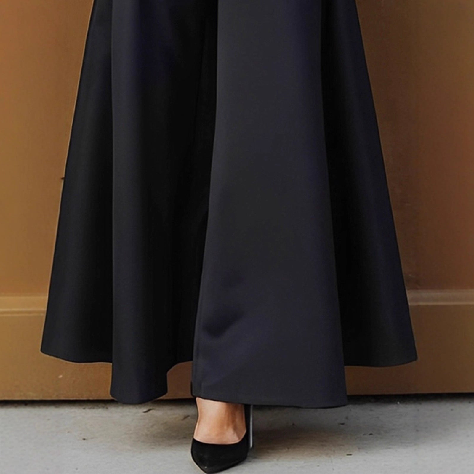 Black wide-leg pants being worn against a brown wall.
