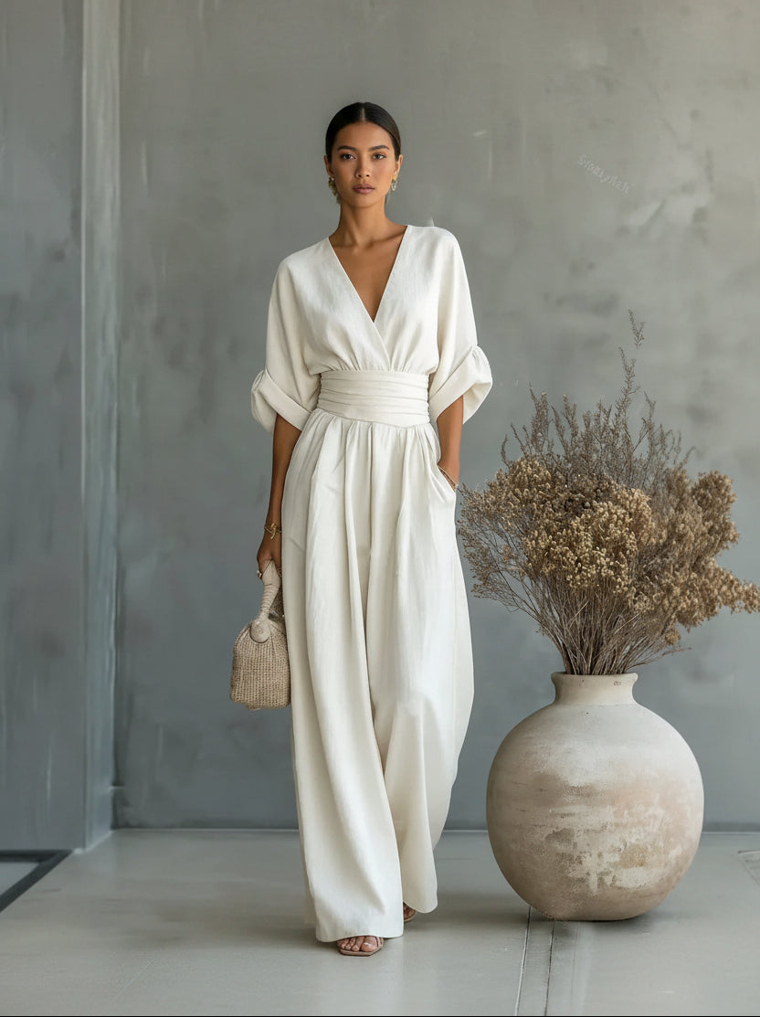 Woman in a white dress standing next to a vase with dried flowers against a gray wall.