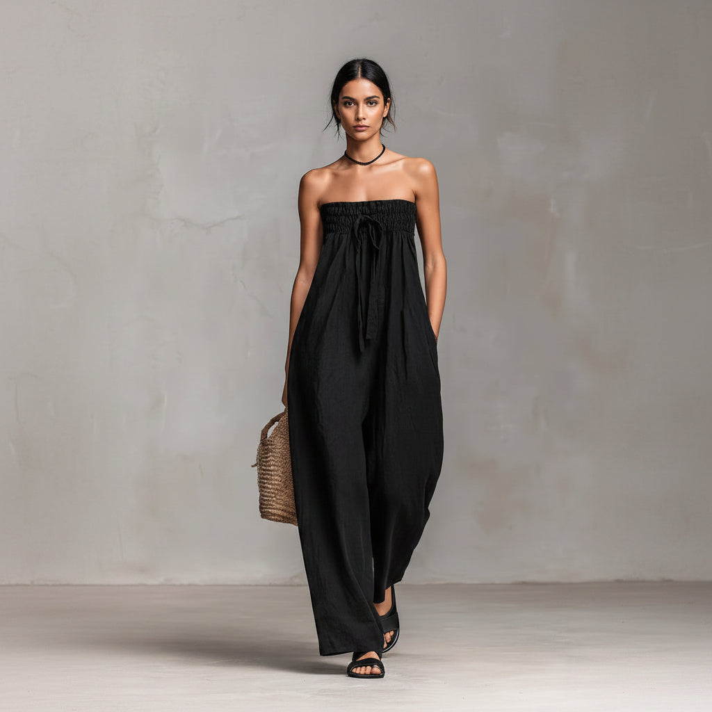 Woman wearing a black strapless jumpsuit holding a woven bag against a neutral background
