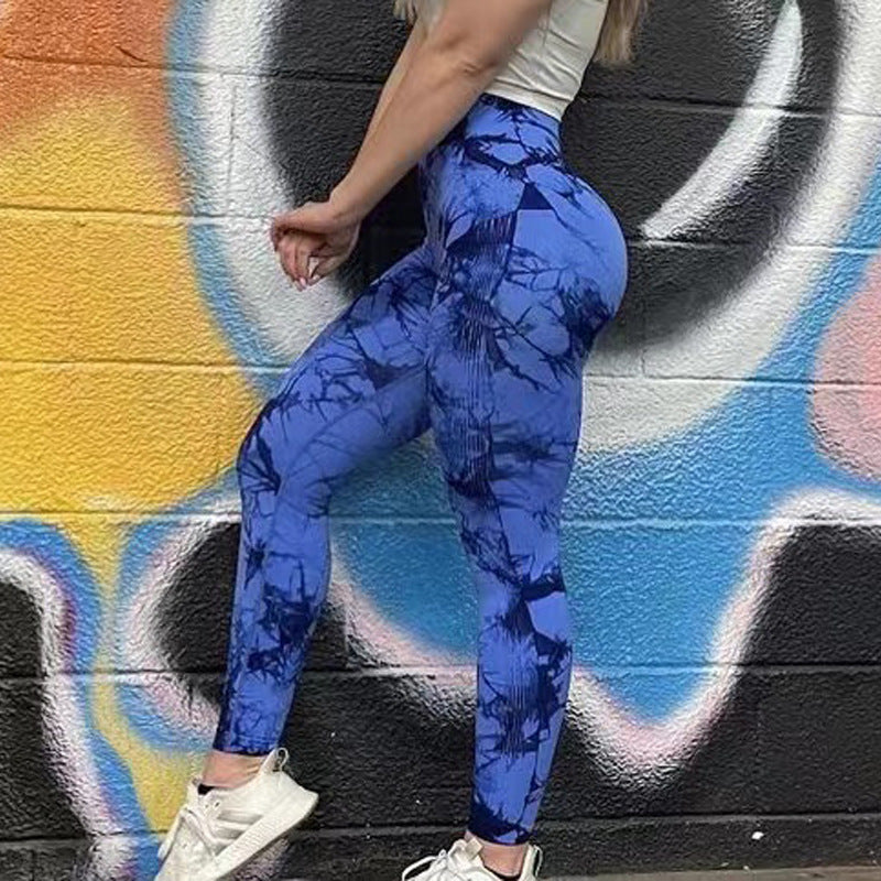Person wearing blue tie-dye leggings standing against a colorful graffiti wall.