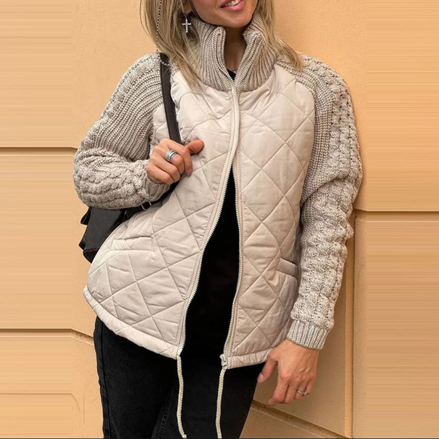Woman wearing a beige quilted jacket with knitted sleeves against a beige wall.