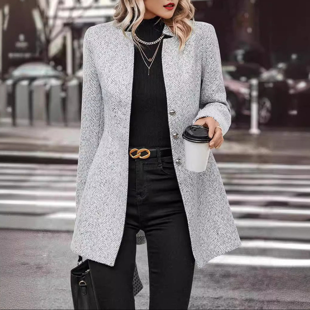 Woman in a gray coat holding a coffee cup on a city street.